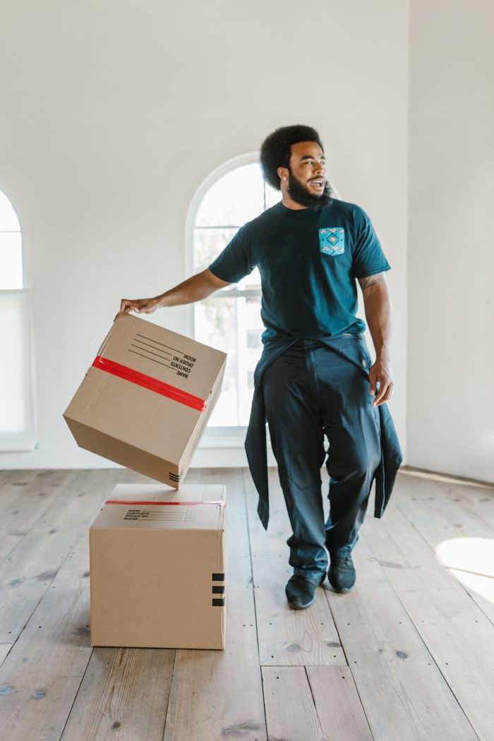 creative-03 A mover carefully handles boxes in a bright, empty room on moving day.