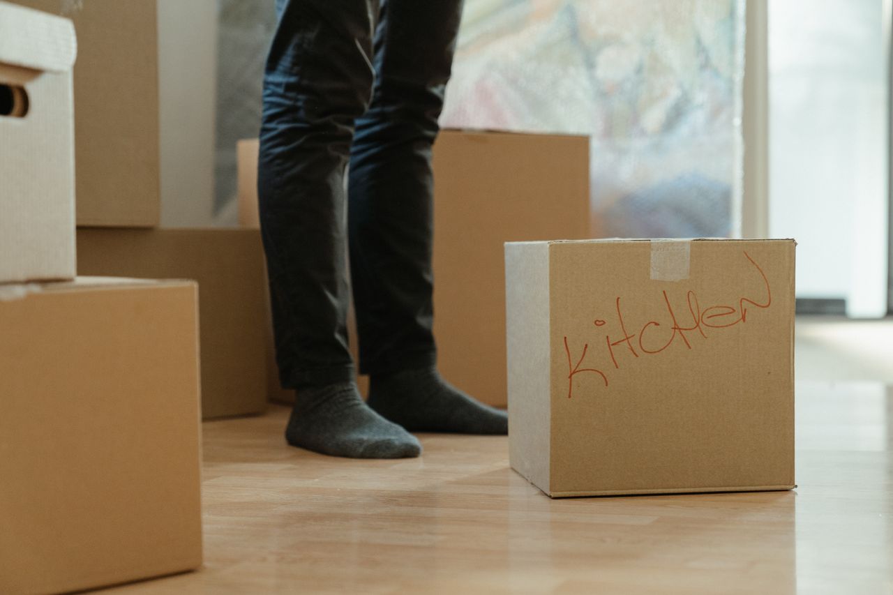 digital Une personne debout dans une pièce entourée de cartons de déménagement étiquetés pour la cuisine.